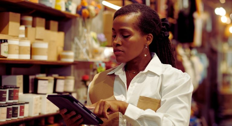 Femme gérant l'inventaire sur tablette devant rayons illustrant le logiciel de gestion de stock